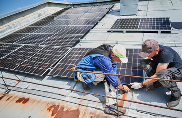 Workers building solar panel system on metal rooftop of house. Two men installers installing...