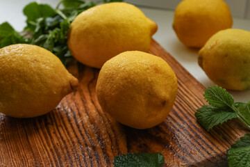 Fresh organic lemons with mint leaves on wooden cutting board