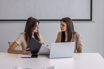 Two businesswomen working on laptop together in the modern office
