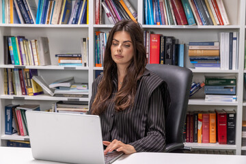 Young businesswoman working on a laptop in the office with book shelf in the background