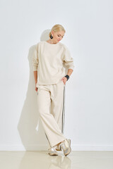 Elegant woman in casual fashion poses indoors against a white wall