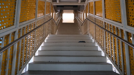 Symmetrical view of a clean pedestrian bridge staircase featuring yellow perforated side panels and metal railings in an urban setting.
