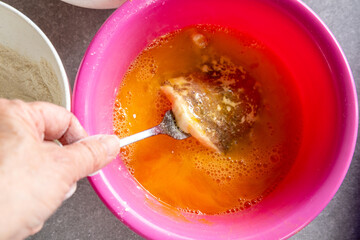 Hand turning floured pork slice in beaten egg with fork
