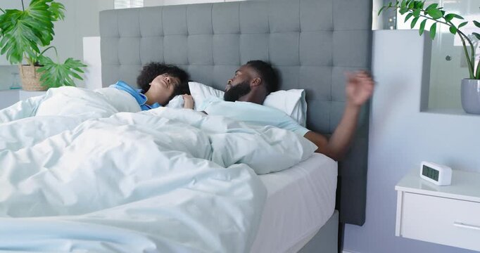 Diverse couple waking at digital alarm ringing turning off and cuddling on white comforter gray bed