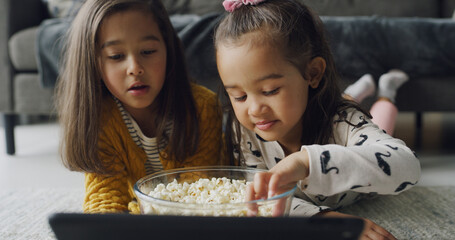 Popcorn, tablet and watching with girls on floor in living room of home for subscription service. App, eating and video streaming with sister kids in apartment together for bonding or entertainment