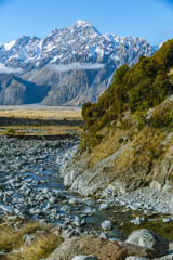 Clear stream flows through rocky terrain with towering snow-covered mountains behind.