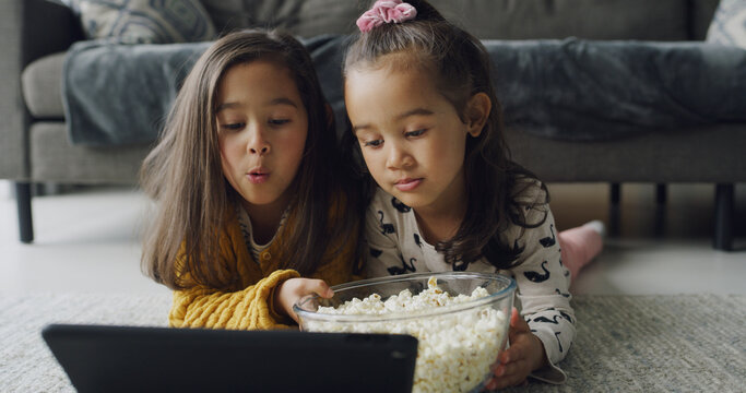 Children, sister or watching with tablet in home for online entertainment or subscription. People, girl or siblings streaming with technology or popcorn for movie, snack or bonding together on floor - Powered by Adobe