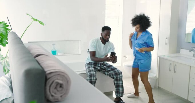 Diverse couple starting morning in master bath, checking smartphone texts while brushing teeth