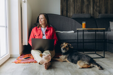 Freelancer woman working from home with laptop, sitting on floor in cozy living room, barefoot and...