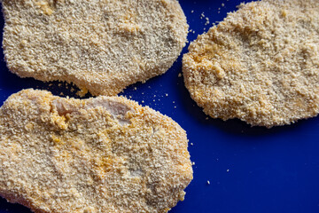 Three breaded raw pork slices on dark blue tray, top view