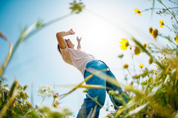Summer mood. a young and cheerful guy dances against a background of blue sky and flowers. A...