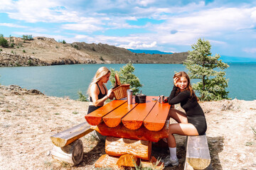 Tourists enjoy a sunny day by the lake while relaxing at a wooden picnic table