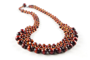 A close-up of a necklace made of wooden beads. The beads are a mix of red and brown hues, and they...