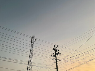 Silhouette of utility poles and electric wires against a pastel sunset sky, perfect for urban,...