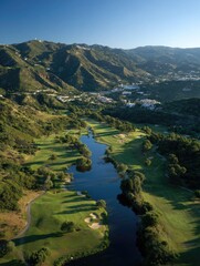 Aerial view of a golf course nestled in a valley, with a lake winding through.  Mountains and distant town in background