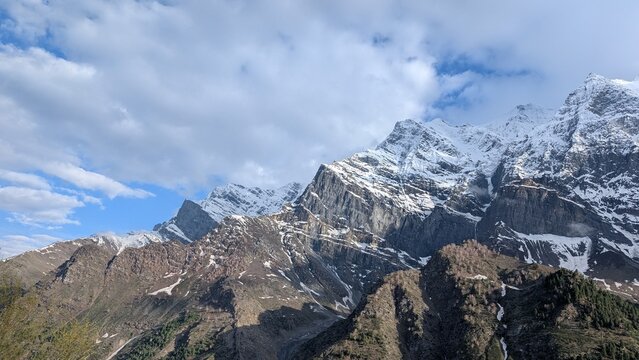 panoramic view of snow filled mountains with texture and clouds in the bright blue sky 