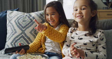 Pointing, popcorn and watching TV with girls on sofa in living room of home together for streaming....