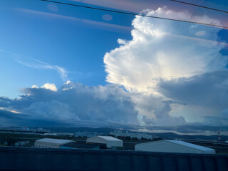 青空に浮かぶ積乱雲と新幹線の車窓から見た工業地帯の風景