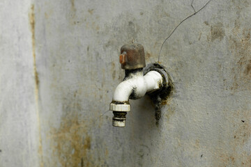 Close-up shot of an old outdoor water faucet mounted on a weathered wall, showing moss growth,...