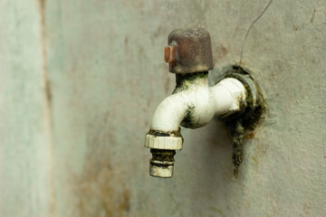 Close-up shot of an old outdoor water faucet mounted on a weathered wall, showing moss growth,...