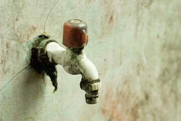 Close-up shot of an old outdoor water faucet mounted on a weathered wall, showing moss growth, dirt, and signs of aging. Perfect for illustrating plumbing issues, maintenance, water supply, and urban 
