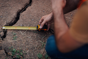 Construction worker measuring crack in ground with tape measure