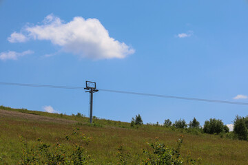 ​A scenic summer landscape features a green hillside with a ski lift tower set against a deep...