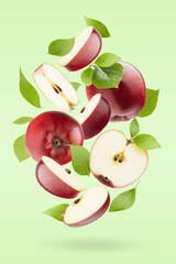 Ripe red apples with green leaves fly as swirl on pastel green white background as art composition, with whole, half, quarter fruit, shadow. Summer juicy fruits for advertising, design, label product.