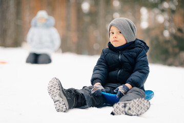 Child sitting on a blue sled in snowy forest enjoying winter fun