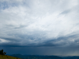A sweeping view of green hills and distant mountains under a stormy sky, perfect for travel ads,...