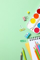 Vertical photo of school supplies including notebook, pencils and stationery on green background