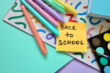 Flat lay composition of colorful school and art supplies arranged around a small easel with a blank canvas, set on pastel-colored paper background. Ideal for themes of back to school, creative