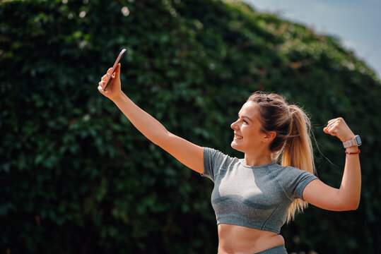 Young sporty woman taking selfie showing biceps after workout outdoors