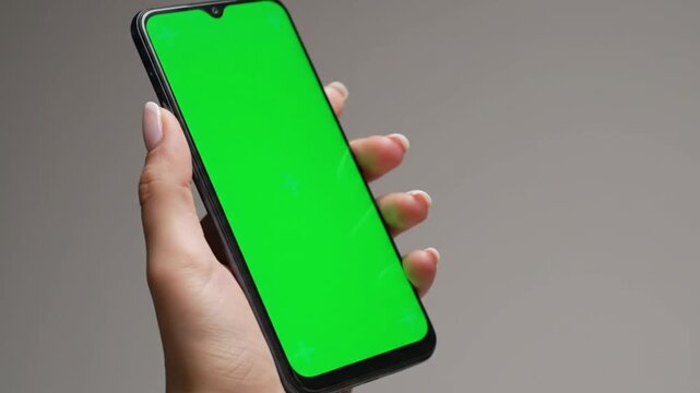 Close up female hand holding smartphone with green screen display on neutral background