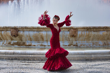 A beautiful woman dancing flamenco in a square in Seville, Spain. She is wearing a red dress with...