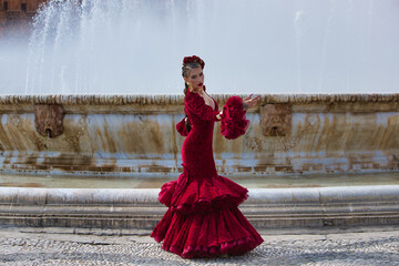 A beautiful woman dancing flamenco in a square in Seville, Spain. She is wearing a red dress with...