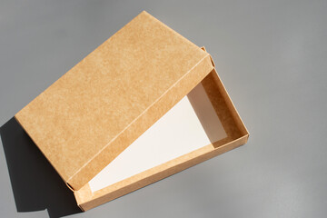 Fototapeta premium Open brown cardboard box on gray surface in direct sunlight with shadow