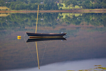 A sailboat floats serenely on a calm lake, its reflection mirrored in the water, with a backdrop of...
