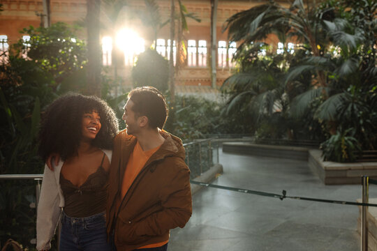 Happy multiracial couple smiling and walking in botanical garden
