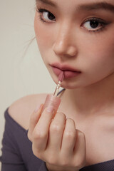 Close-up of a young woman applying lipstick with a delicate expression.