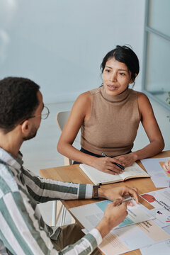 Young businesswoman discussing cooperation with partner during business meeting while they sitting at table with documents