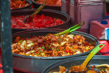 A vibrant close-up of a sizzling stir-fry sweet and sour chicken, displayed in a large pan at Brick Lane Market in London