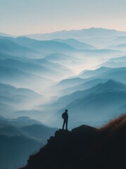A lone figure overlooks a misty, layered mountain range at dawn or dusk