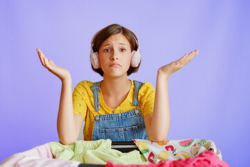 Surprised female in headphones spreading arms by clothes on white background for shopping campaigns