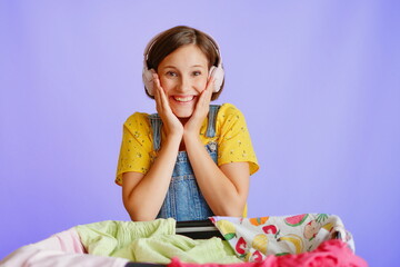 Joyful girl in headphones smiling by clothes on white background for shopping campaigns