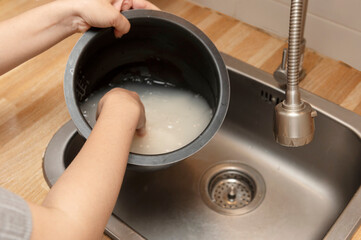 Washing rice in rice cooker pot over kitchen sink.
