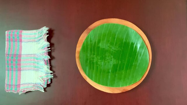 4K top view of hands lift golden sesame onde-onde from banana leaf plate. Crisp outside, sweet mung bean inside. Ideal for Asian food, heritage, and festive culinary visuals.