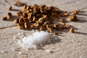 Close-up of coarse sugar crystals and instant coffee granules scattered on a wooden surface.