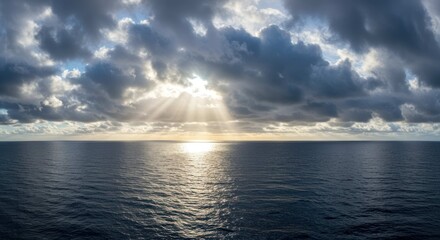 Sun rays break through clouds over a dark ocean horizon.