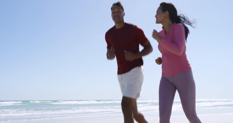 Diverse couple wearing sportswear jogging along beach slowing into warm-up stretches after run - Powered by Adobe